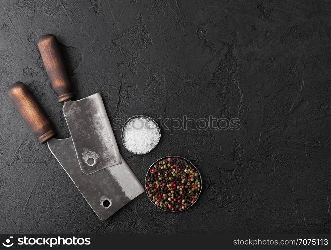 Vintage meat knife hatchets on black stone table background. Butcher utensils. Salt and pepper.