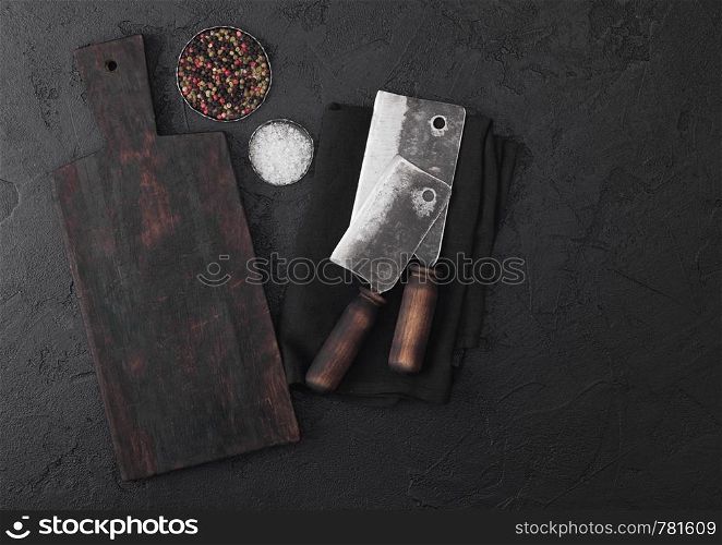 Vintage meat knife hatchets with vintage chopping board and black stone table background. Butcher utensils
