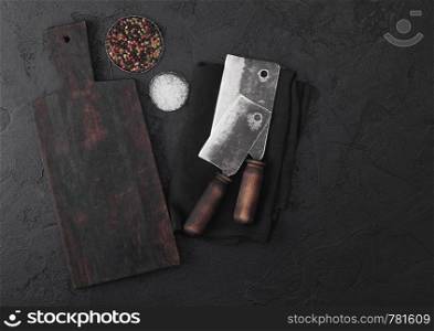 Vintage meat knife hatchets with vintage chopping board and black stone table background. Butcher utensils