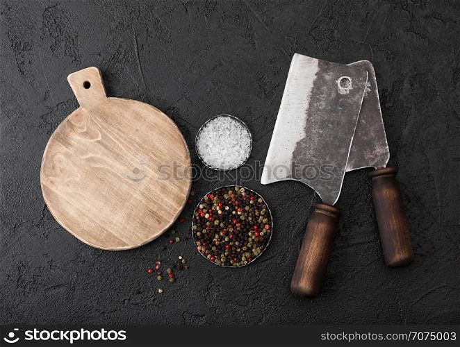 Vintage meat knife hatchets with vintage chopping board and black table background. Butcher utensils. Close up.