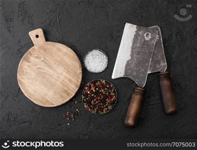 Vintage meat knife hatchets with vintage chopping board and black table background. Butcher utensils. Close up.