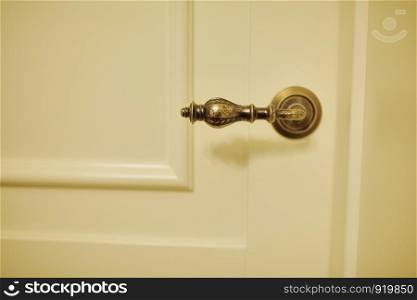 Vintage metal bronze handle in a wooden white door.. Vintage metal bronze handle in a wooden white door