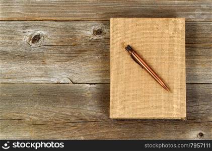 Vintage metal pen and burlap covered notepad on rustic wooden desktop.