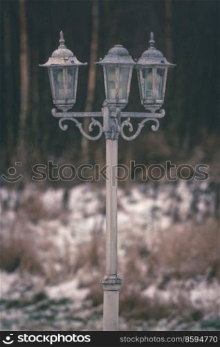 Vintage outdoor lamp with three lanterns containing light bulps in the winter