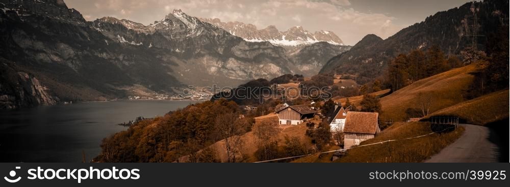 Vintage panoramic view over the lake Walensee and the surrounding hills and villages, with the Swiss Alps in background and a dramatic gray sky. Picture taken in the village Unterterzen, Switzerland.