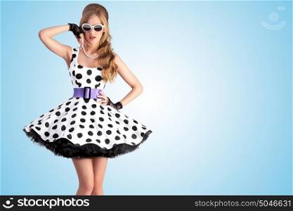 Vintage photo of a beautiful pin-up girl wearing a retro polka-dot dress and sunglasses, posing on blue background.