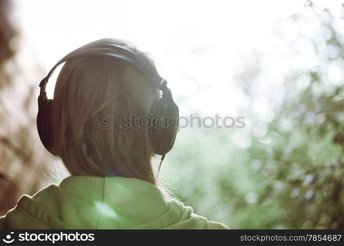 Vintage photo of a woman in headphones listening to music outdoor against bright sunlight. Instagram style color toned