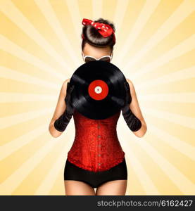 Vintage photo of glamorous pinup girl wearing long gloves and dressed in a red sexy corset, hiding behind LP vinyl record on colorful abstract cartoon style background.