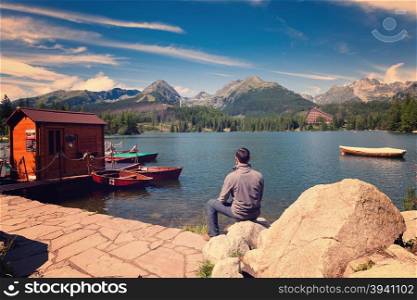 Vintage photo of Man sitting near alpine mountain lake