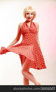 Vintage pinup style. Beautiful stylized young woman dancing. Attractive girl in blond wig and retro spotted red dress on pink. Disguise. Party. Studio shot.