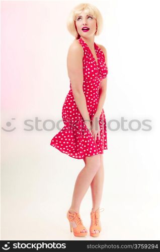 Vintage pinup style. Full length of beautiful stylized young woman. Attractive girl in blond wig and retro spotted red dress on pink. Disguise. Studio shot.