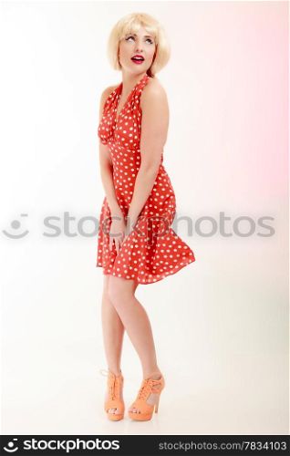 Vintage pinup style. Full length of beautiful stylized young woman. Attractive girl in blond wig and retro spotted red dress on pink. Disguise. Studio shot.