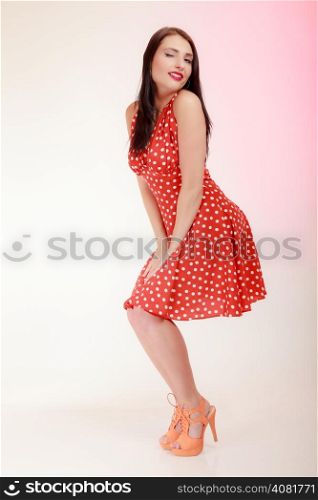Vintage pinup style. Full length of beautiful stylized young woman winking. Attractive brunette girl in retro spotted red dress on pink. Old fashion. Studio shot.