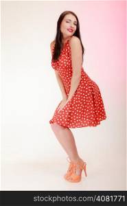 Vintage pinup style. Full length of beautiful stylized young woman winking. Attractive brunette girl in retro spotted red dress on pink. Old fashion. Studio shot.