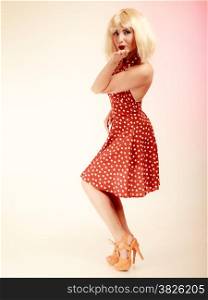 Vintage pinup style. Full length of stylish woman blowing a kiss on pink. Girl in blond wig and retro red dress. Disguise. Studio shot.