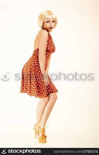Vintage pinup style. Full length of stylish young woman on pink. Attractive girl in blond wig and retro spotted red dress. Disguise. Studio shot.