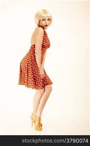Vintage pinup style. Full length of stylish young woman on pink. Attractive girl in blond wig and retro spotted red dress. Disguise. Studio shot.