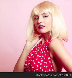 Vintage pinup style. Portrait of beautiful stylized young woman. Attractive girl in blond wig and retro spotted red dress on pink. Disguise. Studio shot.
