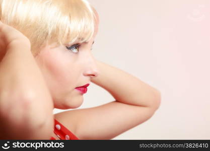 Vintage pinup style. Portrait of beautiful stylized young woman. Face of attractive girl in blond wig and with retro makeup. Disguise. Studio shot.