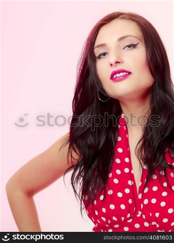 Vintage pinup style. Portrait of beautiful stylized young woman. Attractive brunette girl in retro spotted red dress on pink. Disguise. Studio shot.