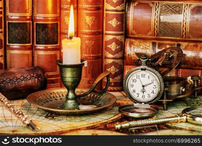 Vintage pocket watch and burning candle in an old candlestick are on the background of antique books