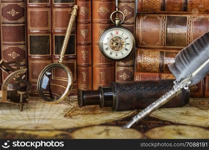 Vintage pocket watch, navigation instruments and silver pen are on the background of antique books