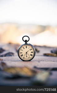 Vintage pocket watch on a wood board, colourful leaves, autumn