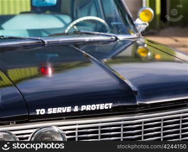 Vintage police car with detail focus on hood and reflections of warning lights in paint