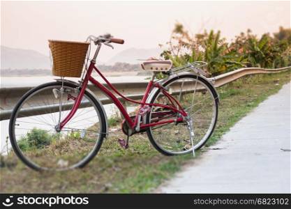 Vintage red bicycle beside river road, stock photo