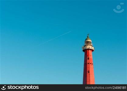 Vintage red iron lighthouse over blue sky background with airplane traces and copy space