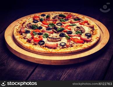 Vintage retro effect filtered hipster style image of ham pizza with capsicum, mushrooms, olives and basil leaves on wooden board on old table