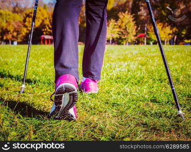 Vintage retro effect filtered hipster style image of nordic walking adventure and exercising concept - woman hiking, legs and nordic walking poles in summer nature