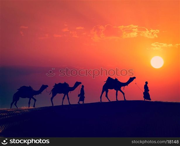 Vintage retro effect filtered hipster style image of Rajasthan travel - two indian cameleers camel drivers with camels silhouettes in dunes of Thar desert on sunset. Jaisalmer, Rajasthan, India