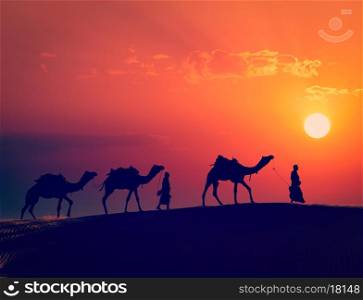 Vintage retro effect filtered hipster style image of Rajasthan travel - two indian cameleers camel drivers with camels silhouettes in dunes of Thar desert on sunset. Jaisalmer, Rajasthan, India