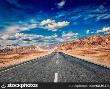 Vintage retro effect filtered hipster style image of road in mountains Himalayas and dramatic clouds on blue sky. Ladakh, Jammu and Kashmir, India. Road in Himalayas with mountains