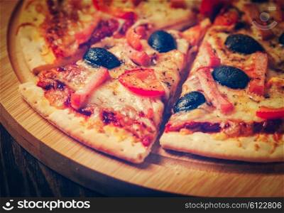Vintage retro effect filtered hipster style image of sliced ham pizza with capsicum and olives on wooden board on table. Ham pizza