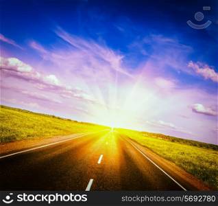 Vintage retro effect filtered hipster style image of travel concept background - road in blooming spring meadow on sunset