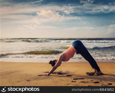 Vintage retro effect filtered hipster style image of Yoga outdoors - young sporty fit woman doing Ashtanga Vinyasa yoga asana Adho mukha svanasana - downward facing dog - at tropical beach on sunset. Kerala, India. Young sporty fit woman doing yoga oudoors at tropical beach
