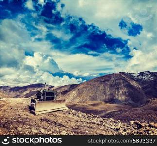 Vintage retro effect filtered hipster style travel image of Bulldozer on road in Himalayas. Ladakh, Jammu and Kashmir, India