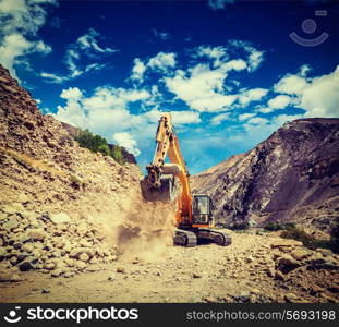 Vintage retro effect filtered hipster style travel image of Excavator doing road construction in Himalayas. Ladakh, Jammu and Kashmir, India
