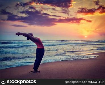 Vintage retro effect hipster style image of young sporty fit woman doing yoga Sun salutation Surya Namaskar pose Hasta Uttanasana on tropical beach on sunset. Young sporty fit woman doing yoga Sun salutation Surya Namaskar