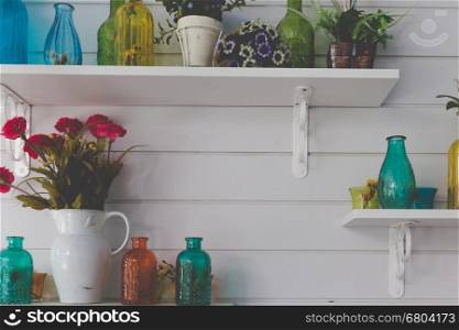 vintage retro glass bottle, flower in vase decorating on shelf on white wall