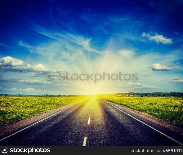 Vintage retro hipster style travel image of travel concept background - road in blooming spring meadow on sunset