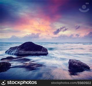 Vintage retro hipster style travel image of tropical beach vacation background - waves and rocks on beach on sunset with beautiful cloudscape