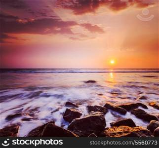 Vintage retro hipster style travel image of tropical beach vacation background - waves and rocks on beach on sunset with beautiful cloudscape