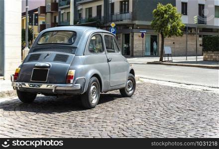 Vintage small car on traditional italian paved street. Dark grey old car.