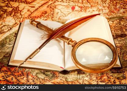Vintage still life - magnifying glass, old book and goose quill pen lying on an old map in 1565.