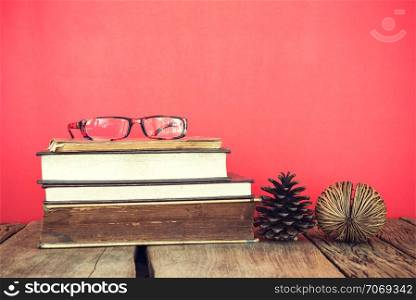 Vintage still life of stack of old books with glass and pine seed on red or pink background.