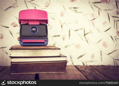 Vintage still life of stack of old books with old camera on sweet color paper background.