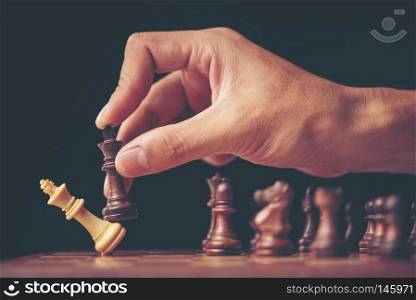 vintage style image of a businessman with clasped hands planning strategy with chess figures on an old wooden table.